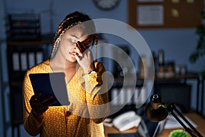 African american woman with braids working at the office at night with tablet tired rubbing nose and eyes feeling fatigue and