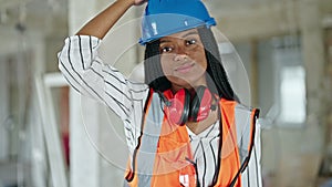 African american woman builder smiling confident wearing hardhat at construction site