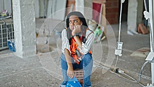 African american woman builder tired holding hardhat sitting on floor at construction site