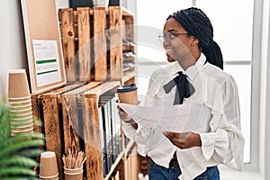 African american woman business worker reading document drinking coffee at office