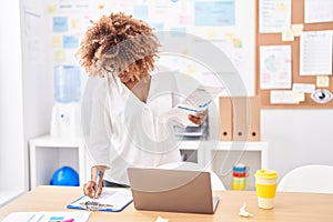 African american woman business worker reading document writing on paperwork at office