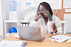 African american woman business worker talking on smartphone drinking coffee at office