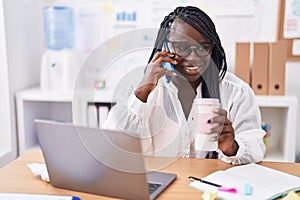 African american woman business worker talking on smartphone drinking coffee at office