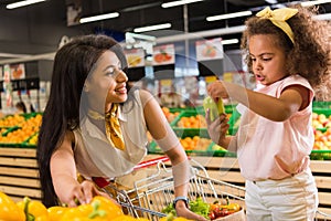 african american woman with child holding bell pepper in grocery