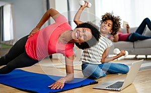 African american woman with child watching online video sports training, stretching on fitness mat.