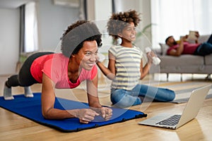 African american woman with child watching online video sports training, stretching on fitness mat.