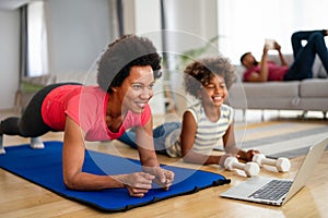 African american woman with child watching online video sports training, stretching on fitness mat.