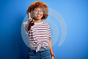 African American woman with curly hair on vacation wearing summer hat and striped t-shirt smiling friendly offering handshake as