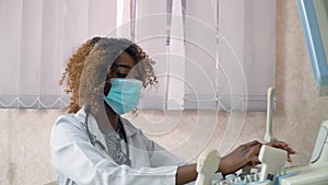 African american woman doctor in protective mask examines patient in ultrasound device monitor. Coronavirus diagnosis