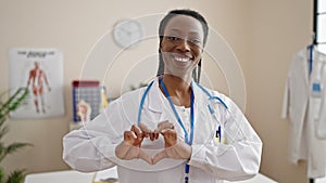 African american woman doctor smiling confident doing heart gesture at clinic