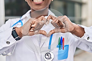 African american woman doctor smiling confident doing heart gesture with hands at hospital