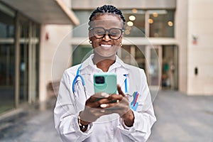 African american woman doctor smiling confident using smartphone at hospital