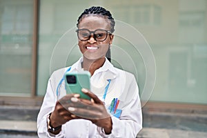African american woman doctor smiling confident using smartphone at hospital