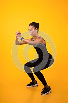 African American Woman Doing Deep Squat Exercise Over Yellow Background