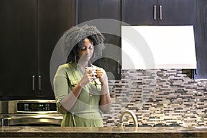 African American Woman Drinking Coffee or CBD Tea in a Kitchen