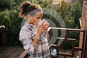 African American woman drinking coffee on her balcony on summer day