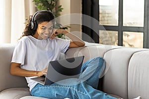 African American woman in earphone with Afro hair using a laptop talking to webcam with friend online