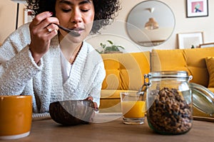 African American woman eating granola for breakfast at home living room. Coffee and orange juice, Copy space.