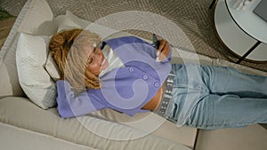 African American woman ethnic girl lying down on couch relax on soft comfortable sofa rest relaxing using mobile phone