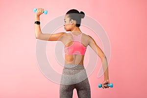 African American Woman Exercising With Dumbbells Over Pink Background, Rear-View