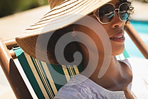 African American woman with hat and sunglasses relaxing on sun lounger in her backyard