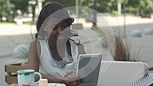 African american woman have video conferance on her tablet sitting in outside cafe