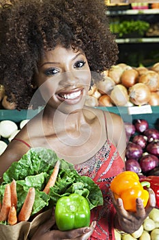 African American woman holding bell peppers and vegetables at supermarket