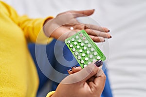 African american woman holding birth control pills sitting on bed at bedroom