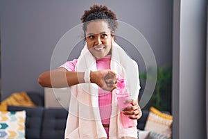 African american woman holding bottle of water looking stopwatch at home