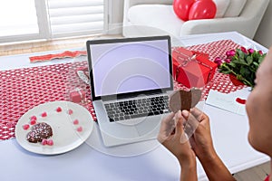 African american woman holding heart shaped cookie on videocall on laptop at home