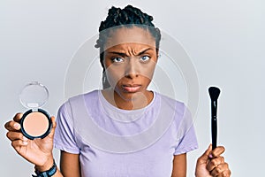 African american woman holding makeup brush and blush skeptic and nervous, frowning upset because of problem