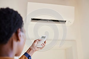 African american woman holding remote control aimed at air conditioner