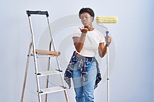 African american woman holding roller painter looking at the camera blowing a kiss with hand on air being lovely and sexy