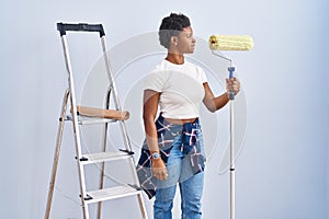 African american woman holding roller painter looking to side, relax profile pose with natural face and confident smile