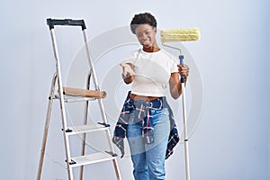 African american woman holding roller painter smiling cheerful offering palm hand giving assistance and acceptance