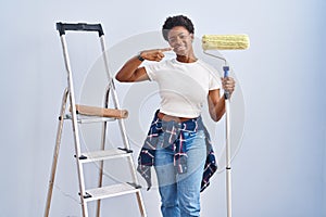African american woman holding roller painter smiling cheerful showing and pointing with fingers teeth and mouth