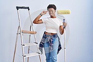 African american woman holding roller painter smiling pointing to head with one finger, great idea or thought, good memory