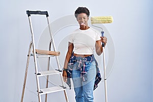 African american woman holding roller painter sticking tongue out happy with funny expression