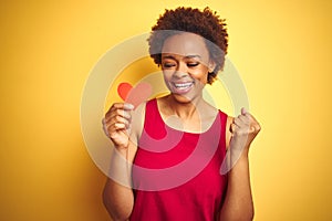 African american woman holding romantic paper hearts over yellow isolated background screaming proud and celebrating victory and