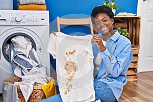 African american woman holding t shirt with dirty stain smiling with a happy and cool smile on face