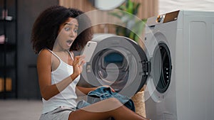 African American woman housewife sad upset shocked biracial ethnic girl pull out of washing machine laundry take jeans