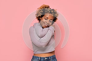 African american woman hugging herself being happy and positive, smiling confident