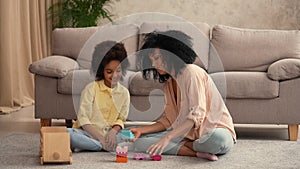 African American woman and litle girl played with wooden toy car and build tower from construction set. Mother and