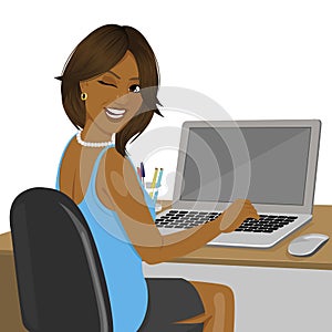 African american woman looking over shoulder sitting in office with laptop winking