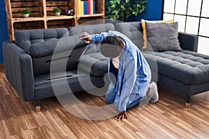 African american woman looking for under sofa at home