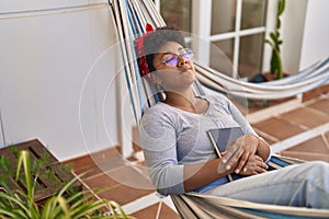 African american woman lying on hammock sleeping at home terrace