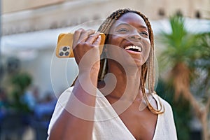 African american woman miling confident listening audio message by the smartphone at coffee shop terrace