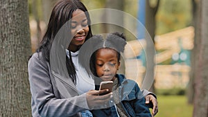 African American woman mother with child daughter little kid girl small baby schoolgirl sitting in park outdoors