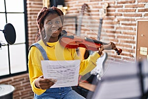 African american woman musician playing violin looking music sheet at music studio