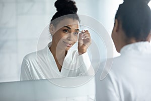 African American woman pinch eyebrows with tweezers in bathroom